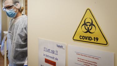 Een foto van een zorgmedewerker in beschermende kleding die een deur opend met waarschuwingen erop