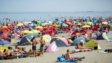 Op deze foto is het strand van Scheveningen te zien, met daarop veel badgasten. Het is druk, veel mensen gebruiken een parasol.