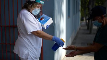 Op deze foto is een vrouw te zien die de handen van een ander met een desinfectiespray bespuit.