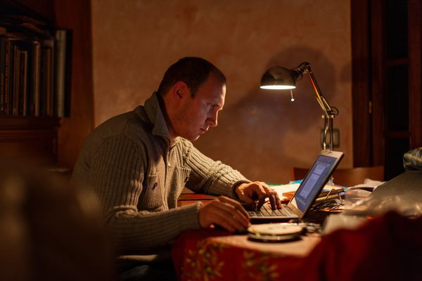 Een foto van een man die in het donker bij lamplicht geconcentreerd op zijn laptop werkt