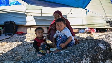 A woman and her children eat under a tarp in an open field in Marapokot, Nagekeo, East Nusa Tenggara, on August 17, 2026, following a 7.7-magnitude earthquake. Thousands of people displaced by a powerful earthquake in eastern Indonesia awaited much-needed aid on August 17 as they camped out at schools, police stations and government offices, with many stuck outside.

JUNI KRISWANTO / AFP