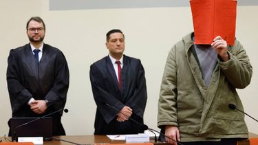 Afghan defendant, partially identified as Farhad N., hides behind a folder next to his lawyers Johann Bund (L) and Omer Sahinci as he arrives in the courtroom at the start of his trial for ramming a car into a crowd in Munich last year, on January 16, 2026 in Munich.

 The suspect, partially identified as Farhad N., is accused of ramming a car into a crowd in Munich last year, killing a two-year-old girl and her mother and injuring dozens. The suspect faces two charges of murder and 44 of attempted murder, with prosecutors saying he acted out of a 