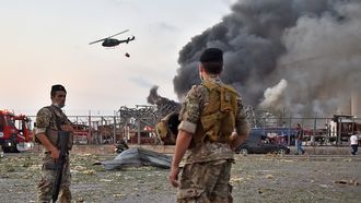 Op deze foto zie je twee Libanese soldaten kijken naar hoe eenhelikopter bezig is de brand te blussen welke ontstaan is door de explosie