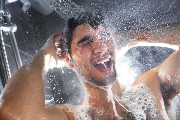 Een foto van een man die onder de douche shampoo uitspoelt