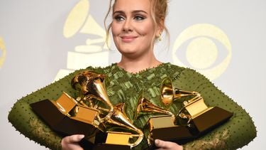 Een foto waarop zangeres Adele te zien is met muziekprijzen in haar armen.