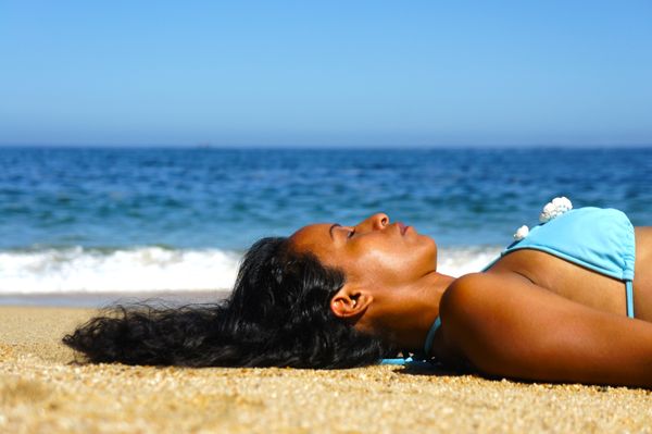 Een vrouw ligt te zonnebaden op het strand in een blauwe bikini.