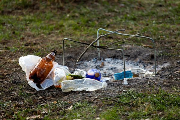 Een foto van afval zoals plastic flesjes bij een uitgebrand kampvuur op gras.