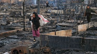 Een vrouw loopt door het verwoeste kamp.