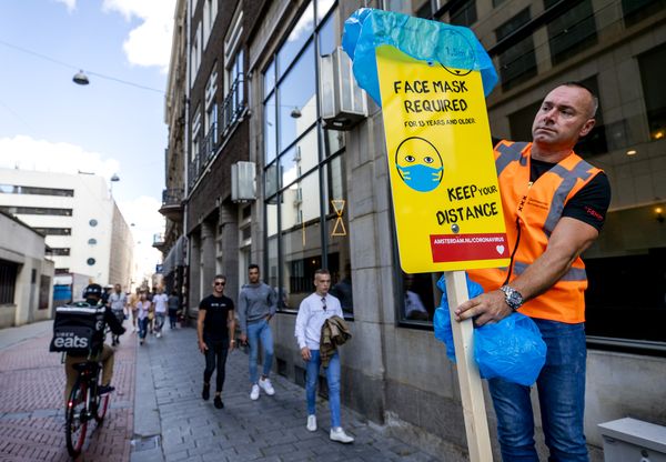Een foto van een man die in Amsterdam een bord plaats met de tekst 'draag een mondkapje'