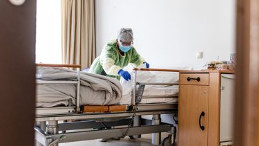 Een foto van een zorgmedewerker aan een ziekenhuisbed.