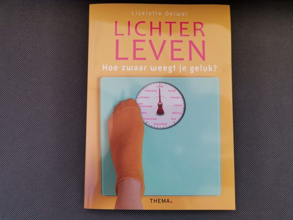 Een foto waarop de cover van het boek Lichter leven. Hoe zwaar weegt je geluk? te zien is. Op de cover staat een weegschaal met woorden zoals 'liefde', 'familie' en 'genieten'.