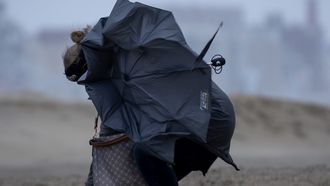 Een foto van een vrouw op het strand met een kapot gewaaide paraplu in de storm, code rood, storm
