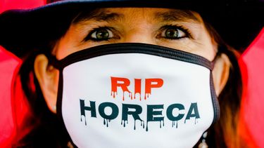 Een foto van een demonstrante met een mondkapje met de tekst RIP horeca