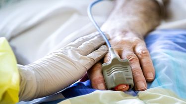 Een foto van een hand van een verpleegkundige op de hand van een coronapatiënt
