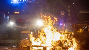 Op deze foto is een brand in de Schilderswijk in Den Haag te zien. Achter het vuur staat een auto van de politie.