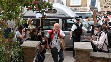 Een foto van Dominic Cummings die tussen fotografen en protestanten door naar zijn huis loopt