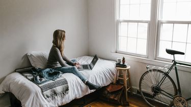 Vrouw zit op haar bed in studentenkamer, kamer