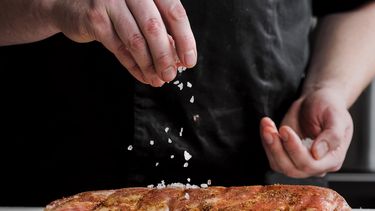 Een foto van twee handen die voedsel met zout bestrooien