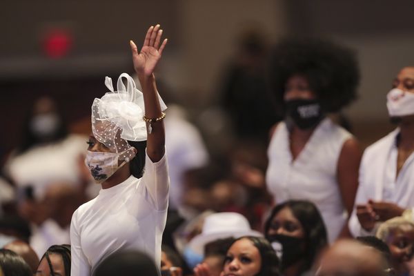 Een foto van een vrouw in het wit die haar hand opsteekt tijdens de begrafenisdienst van George Floyd