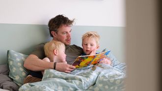 ILLUSTRATIEF - Een vader leest zijn zoontjes voor op bed, thuis in de slaapkamer. ANP ROOS KOOLE
