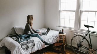 Vrouw zit op haar bed in studentenkamer, kamer