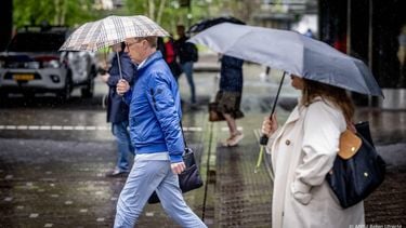 DEN HAAG - Mensen op straat trotseren regen en windstoten. Weerinstituut KNMI heeft voor delen van het land code geel afgegeven. ANP ROBIN UTRECHT