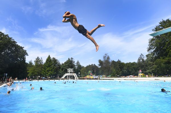 Een foto van een man die van de duikplank in een zwembad springt.