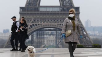 Een foto van een vrouw met hond bij de Eiffeltoren, in Parijs zijn al strenge coronamaatregelen