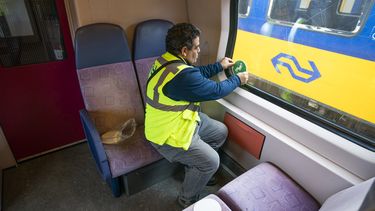 Een monteur van de NS plakt stickers in een trein, die aangeven op welke stoelen wel of niet mag worden gezeten.
