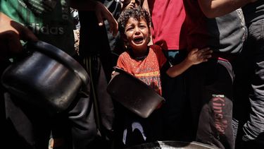 A child cries as Palestinians gather to receive a hot meal at a food distribution point in the Nuseirat camp for refugees in the central Gaza Strip on May 24, 2025. The United Nations chief said on May 23 that Palestinians were enduring 