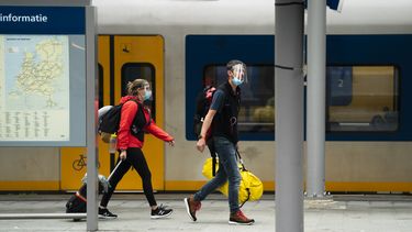 Een foto van twee reizigers op het perron van een treinstation