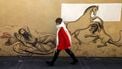 An Iranian woman walks past a mural depicting a scene from the Iranian national epic 