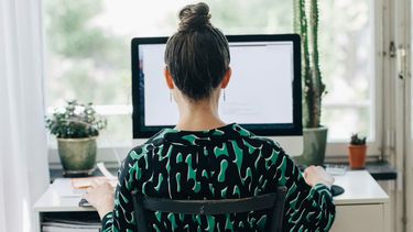Een foto van een vrouw, thuiswerkend achter haar computer