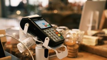 Een betaalterminal op een toonbank, met een bonnetje en achtergrond vol wazige details van een winkelomgeving. kleding uitgaven geld
