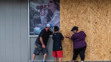 Een foto van drie Amerikanen die houten schotten tegen hun winkel spijkeren.