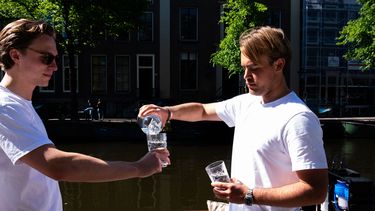 Een foto van twee mannen van Aquablue die Amsterdams grachtenwater drinken.