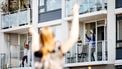 Op deze foto zijn ouderen op hun balkon te zien, daarvoor staat iemand sportoefeningen voor te doen.