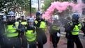 Een foto van politie in zware uitrustig op de straten van Londen, er hangt een roze gaswolk achter ze.