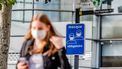 Een foto van iemand in België met een mondkapje op. In de achtergrond staat een bord met 'masker verplicht', in het Frans.