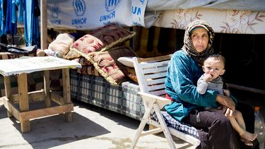 Op deze foto zie je een Syrische vluchtelinge met haar kind op schoot voor een tent.