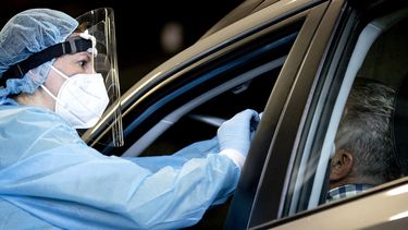 Een foto van een zorgmedewerkster die iemand in een auto test op het coronavirus