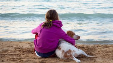Een foto van een meisje en een hond waartegen zij vast vaak ik hou van jou zegt, op het strand