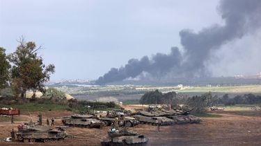 Israeli soldiers stand next to tanks at a position in Israel near the border with the Gaza Strip as smoke billows over the Gaza Strip after Israeli bombardment on January 14, 2024, as the war between Israel and militant group Hamas entered its 100th day. 
Menahem KAHANA / AFP