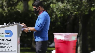 Op deze foto is iemand te zien die briefstemmen in een stembus doet.