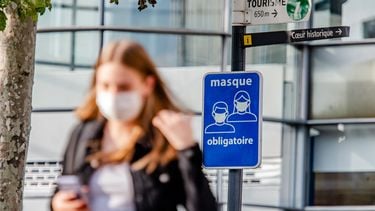 Een foto van iemand in België met een mondkapje op. In de achtergrond staat een bord met 'masker verplicht', in het Frans.