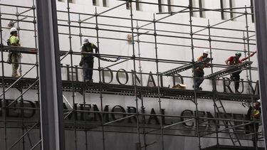 Workers build scaffolding near the signage for the 