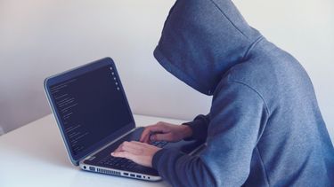 Man met hoodie achter een laptop