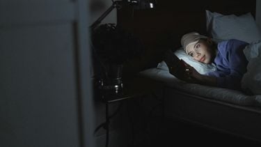 persoon ligt voor het slapen op haar mobiel te kijken en heeft last van blauw licht