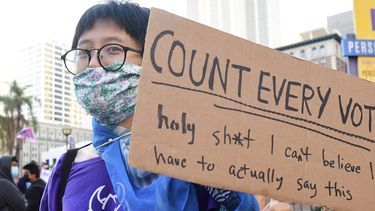 Een vrouw houdt een bord vast met 'count every vote'.