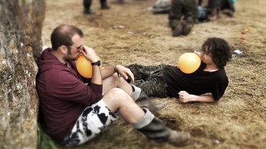 Op deze foto zie je twee mannen op een festival lachgas gebruiken.